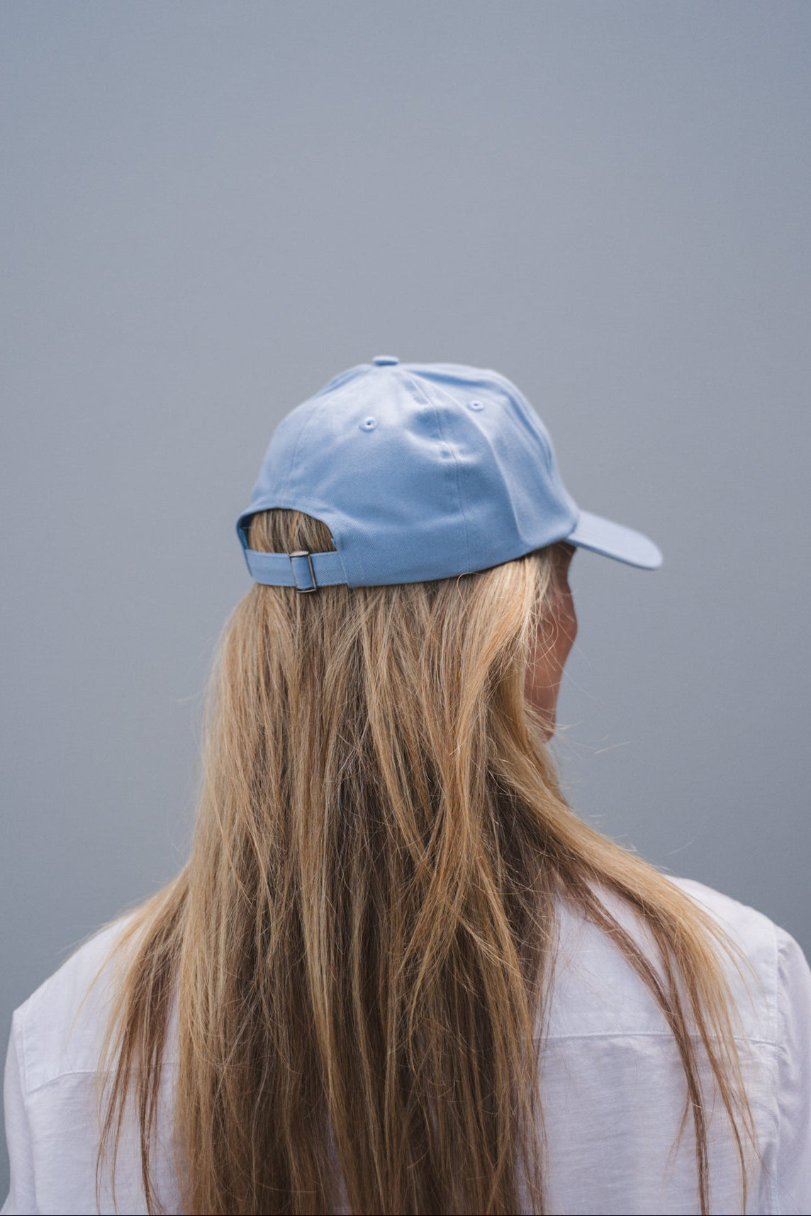 Person wearing a light blue cap and white shirt against a gray background