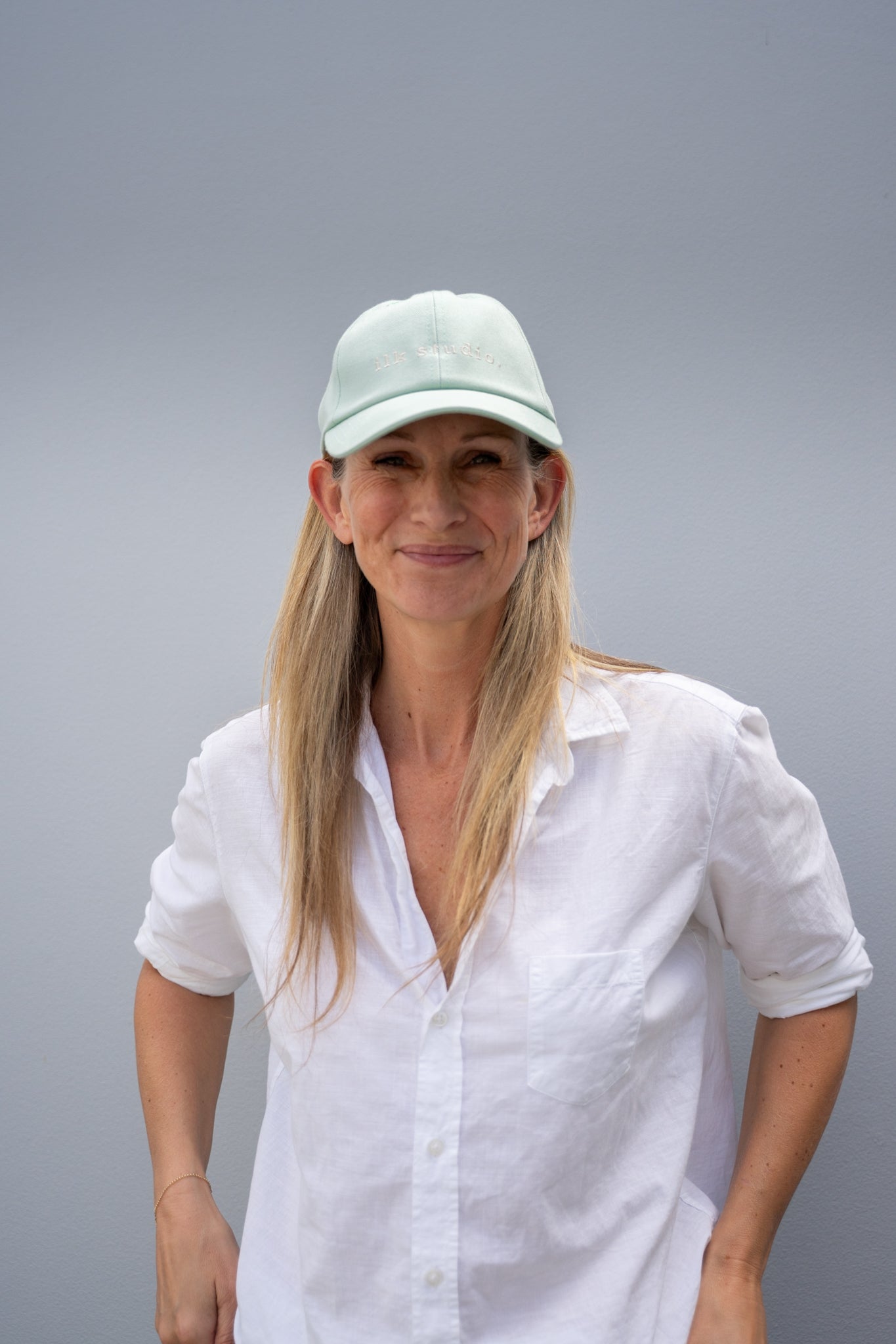 Woman wearing a white shirt and light-colored cap against a gray background