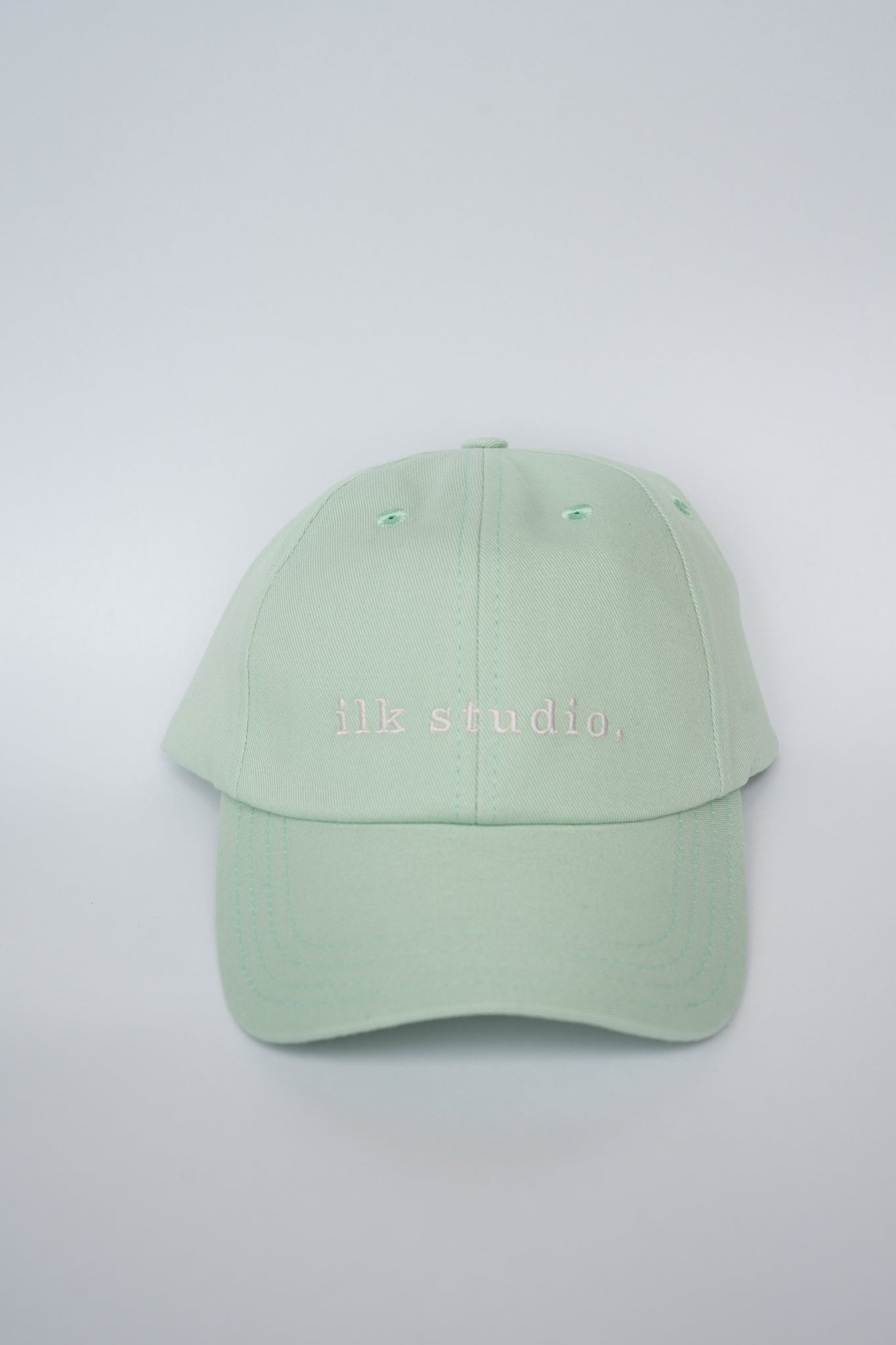 Light green baseball cap with 'MK studio' text on a light gray background