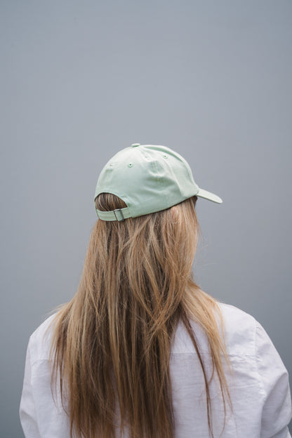 Person wearing a light green cap and white shirt against a gray background